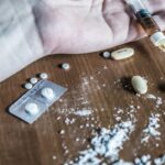 Mano che impugna una siringa e alcune pasticche, anche spezzate e sbriciolate sul tavolo