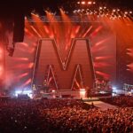 Il palco di un live dei Depeche Mode con luci e scenografie maestose e una grande folla ad assistere al concerto