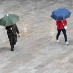 Ombrelli aperti, gente passeggia sotto la pioggia