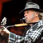 Neil Young con la chitarra e l'armonica durante una esibizione