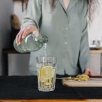 una donna versa acqua in un bicchiere con il limone