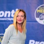 Giorgia Meloni con dietro il simbolo di FdI