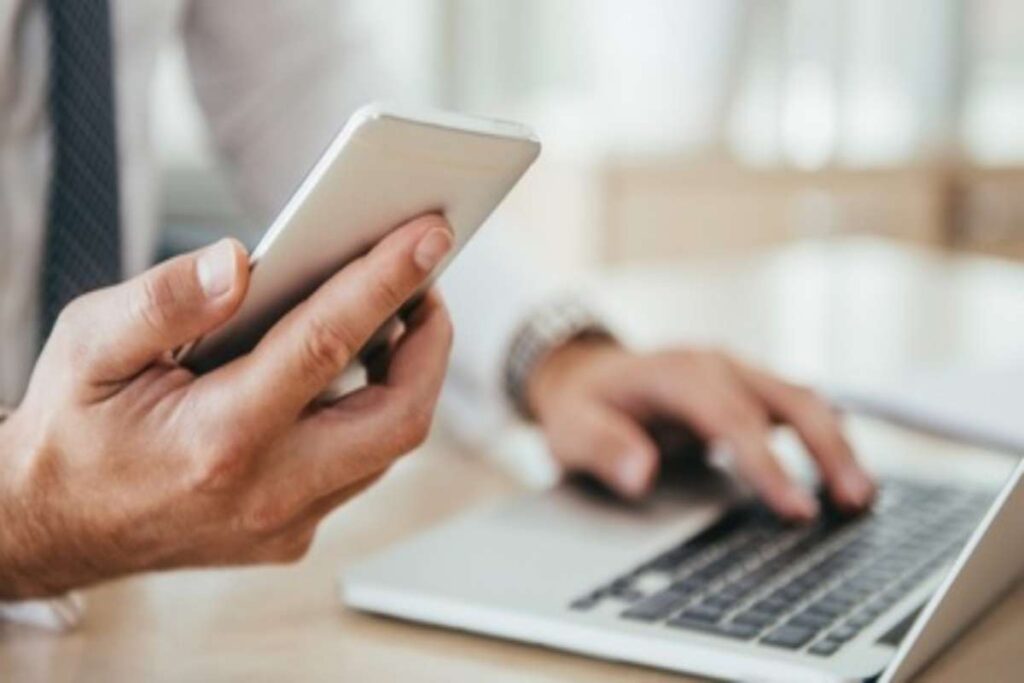 Uomo al computer con telefonino in mano