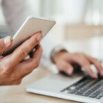 Uomo al computer con telefonino in mano