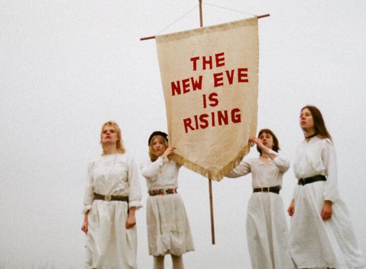 Particolare della copertina dell'abum The New Eve is Rising della band The New Eves. Le quattro componenti del gruppo sono vestite di bianco su sfondo bianco e tengono uno stendardo bianco su cui è scritto il titolo dell'album in rosso