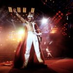 Freddy Mercury in un live, con il suo costume regale in tipico stile glam rock e il resto della band sullo sfondo