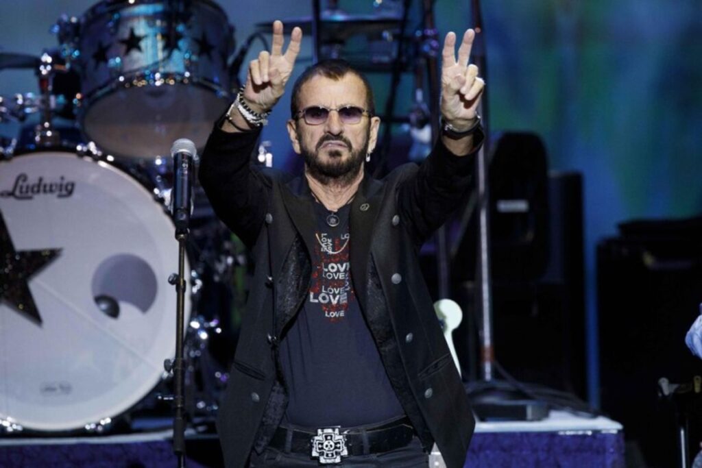Ringo Starr su un palco fa il segno della pace