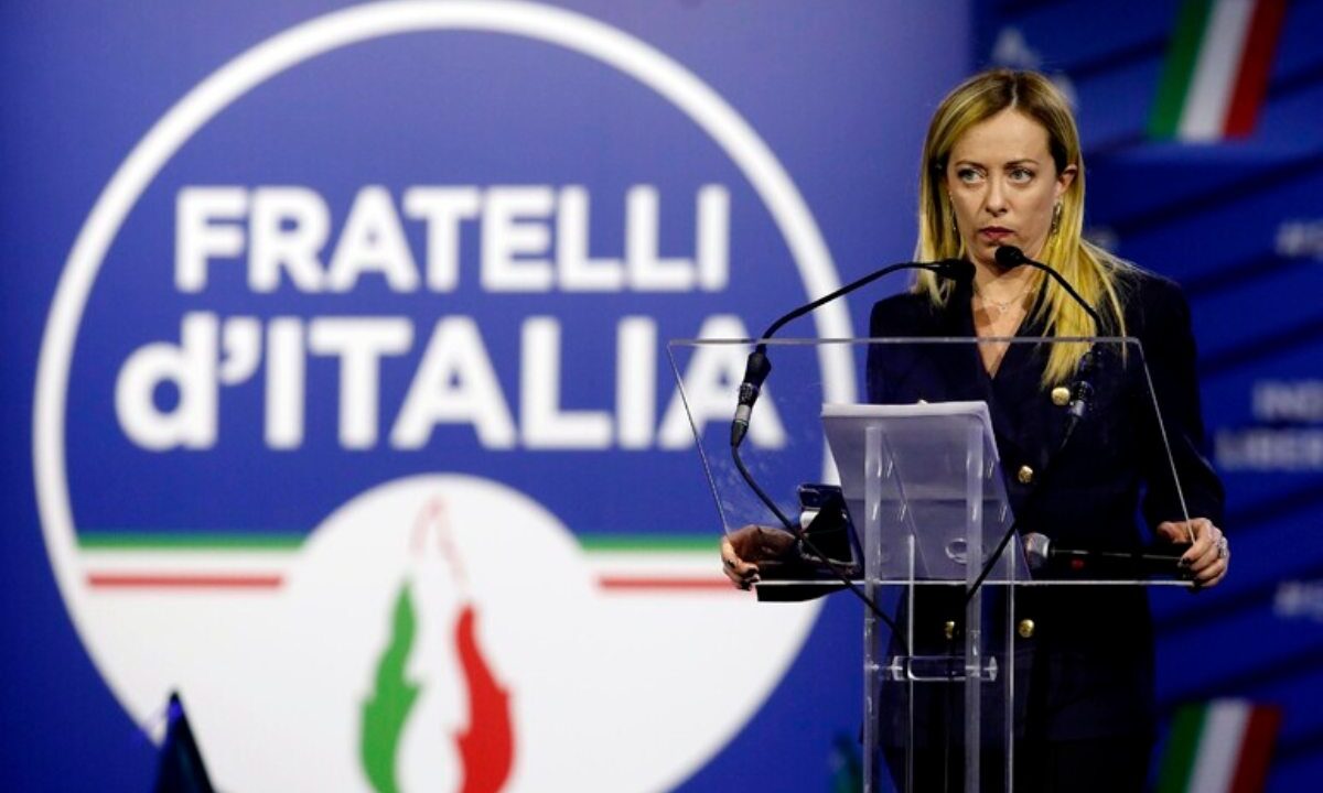 giorgia meloni e il logo fdi alle sue spalle