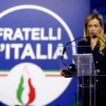 giorgia meloni e il logo fdi alle sue spalle
