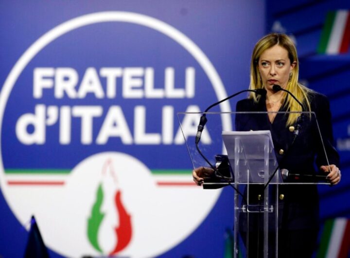giorgia meloni e il logo fdi alle sue spalle