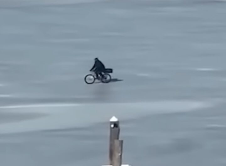 Un uomo attraversa un fiume ghiacciato in bicicletta