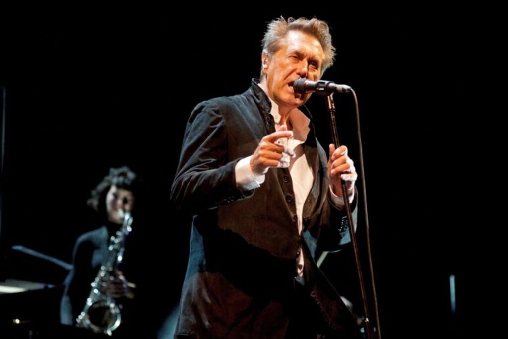 Bryan Ferry, leader dei Roxy Music, mentre canta su un palco con un sassofonista sullo sfondo