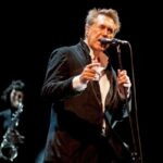 Bryan Ferry, leader dei Roxy Music, mentre canta su un palco con un sassofonista sullo sfondo