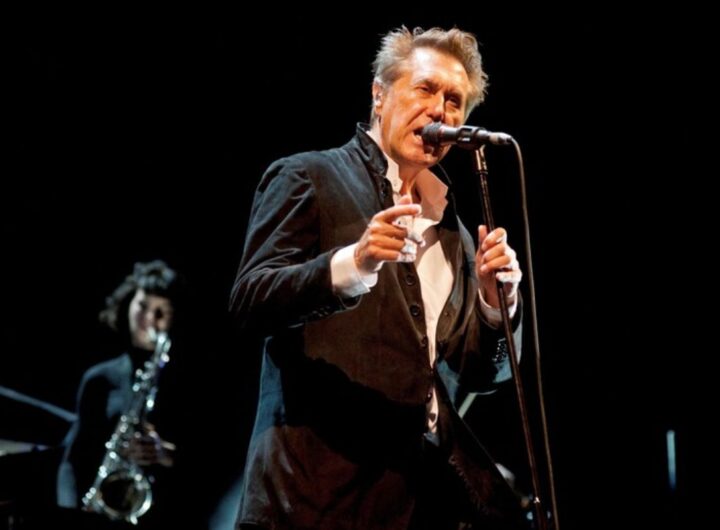 Bryan Ferry, leader dei Roxy Music, mentre canta su un palco con un sassofonista sullo sfondo