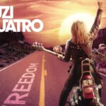 La copertina di Freedom di Suzi Quatro, con la bassista di spalle su una moto, con un basso in braccio, vestita di pelle, su una strada diretta verso il tramonto con la scritta "Freedom" e un braccio alzato verso il cielo