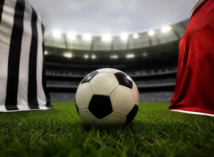 Un maglia bianconera e una rossa di fronte, in mezzo un pallone in un campo da calcio