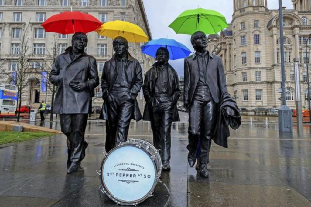 La statua dei Beatles a Liverpool. I Fab Four sono immortalati mentre camminano uno a fianco all'altro. La foto, scattata per i 50 anni di Sgt. Peppers, mostra le statue con ombrelli colorati e una cassa di batteria con una scritta celebrativa sulla pelle