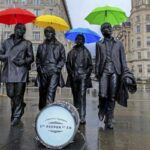 La statua dei Beatles a Liverpool. I Fab Four sono immortalati mentre camminano uno a fianco all'altro. La foto, scattata per i 50 anni di Sgt. Peppers, mostra le statue con ombrelli colorati e una cassa di batteria con una scritta celebrativa sulla pelle
